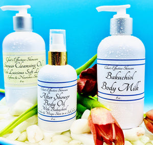 Pampering Shower & Bath Trio/ Three products in a set/ The Shower Cleansing Oil, the After Shower Body Oil, and Bakuchiol Body Milk/ All three products are in white bottles with silver and gold pump tops/In a setting With a blue background, Red Tulips, and pretty white pebbles/ Char's Effective Skincare